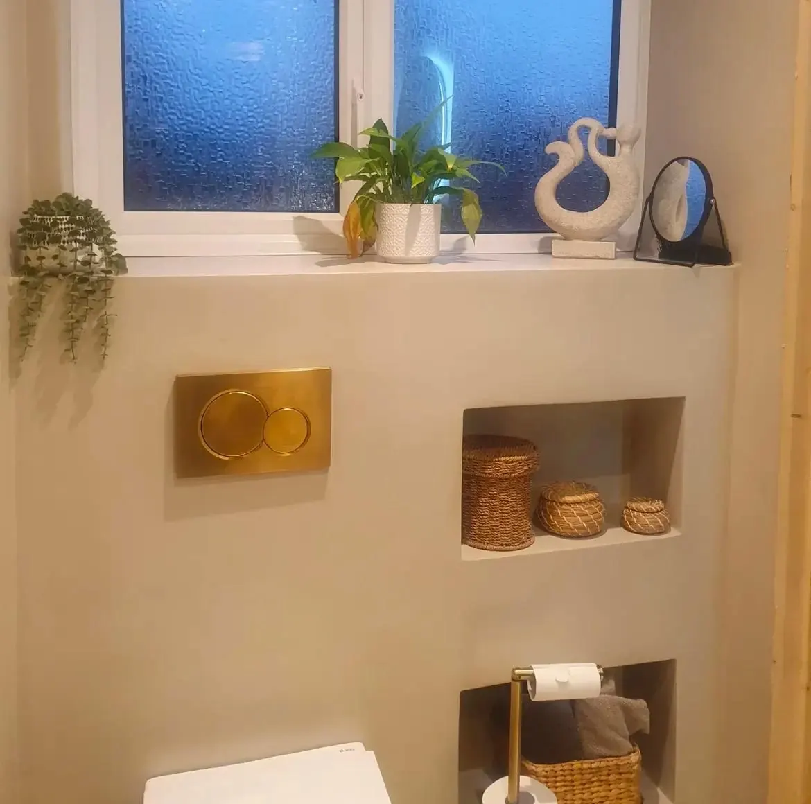 Microcement wall with built-in niches, brushed brass flush plate and a deep window ledge
