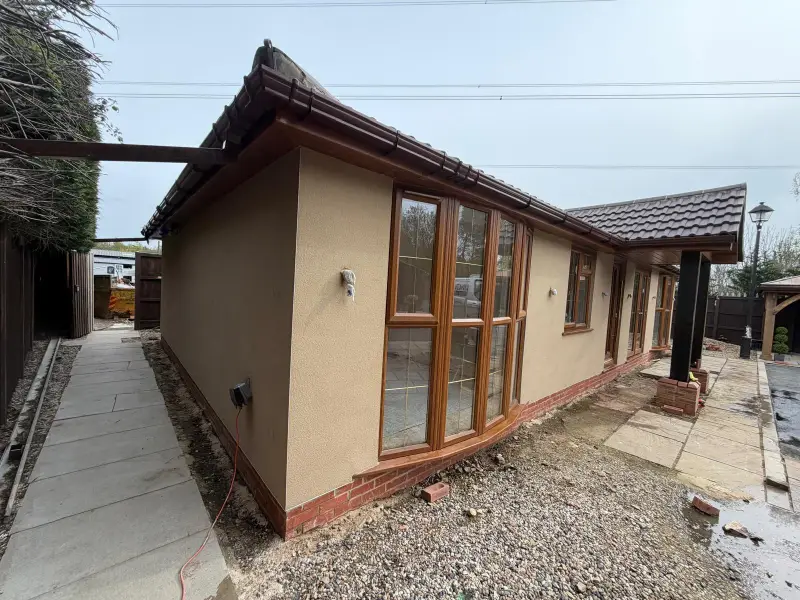 Bungalow finished in warm sandstone silicone render above a red brick plinth