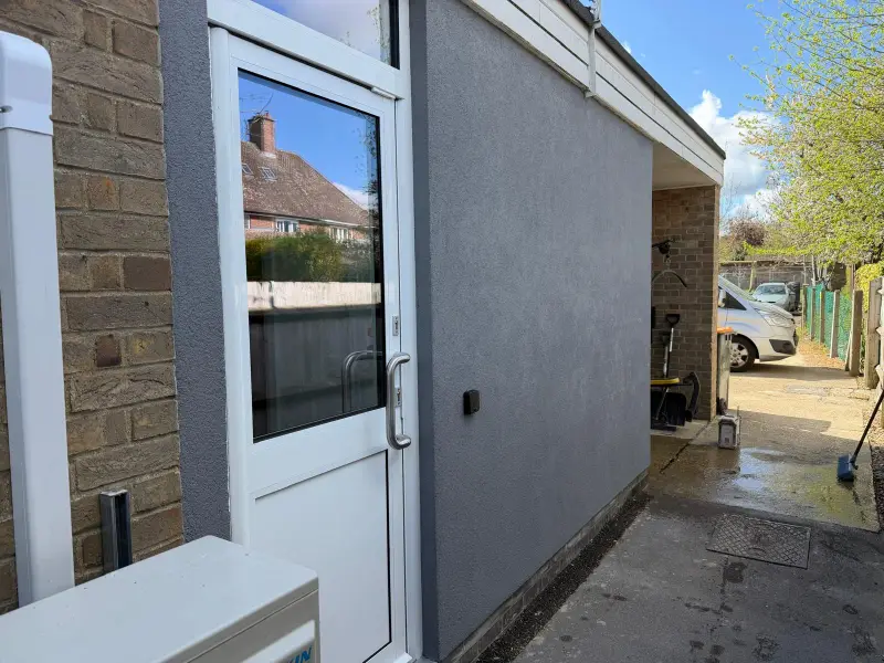Single-storey extension finished in mid-grey textured silicone render beside a white door