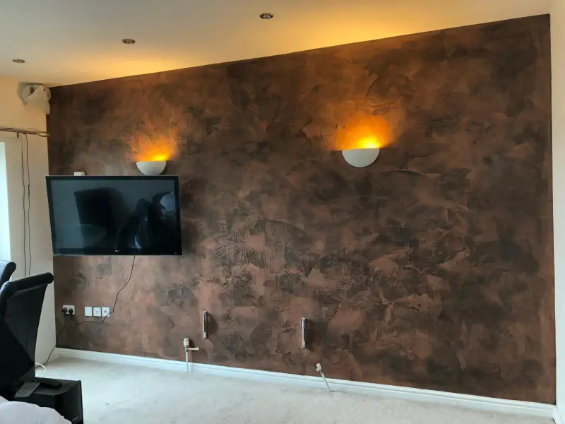 Living room feature wall in bronze metallic Venetian plaster lit by two uplighters