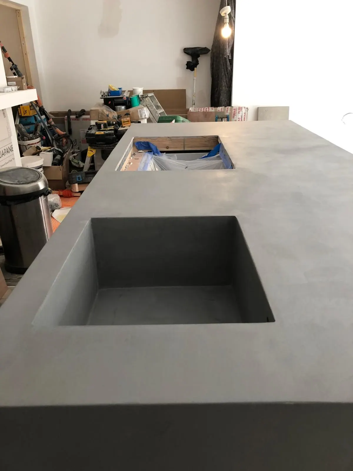 Integrated square sink formed in the grey microcement worktop of a kitchen island